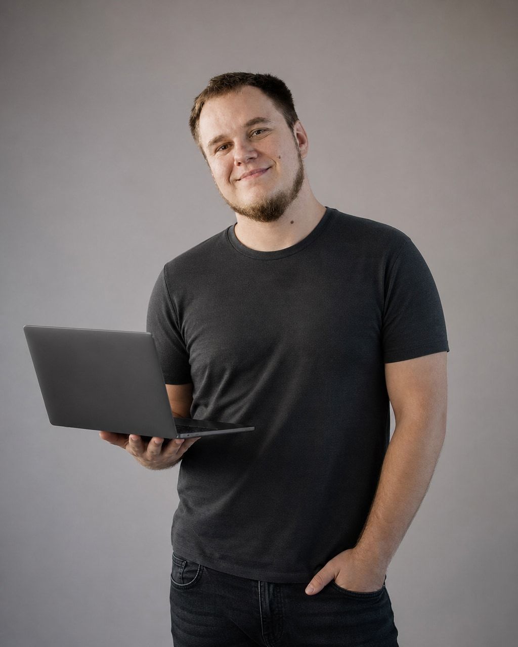 Daniel Siwek, założyciel SyncGrowth, uśmiecha się i trzyma laptopa na szarym tle studyjnym